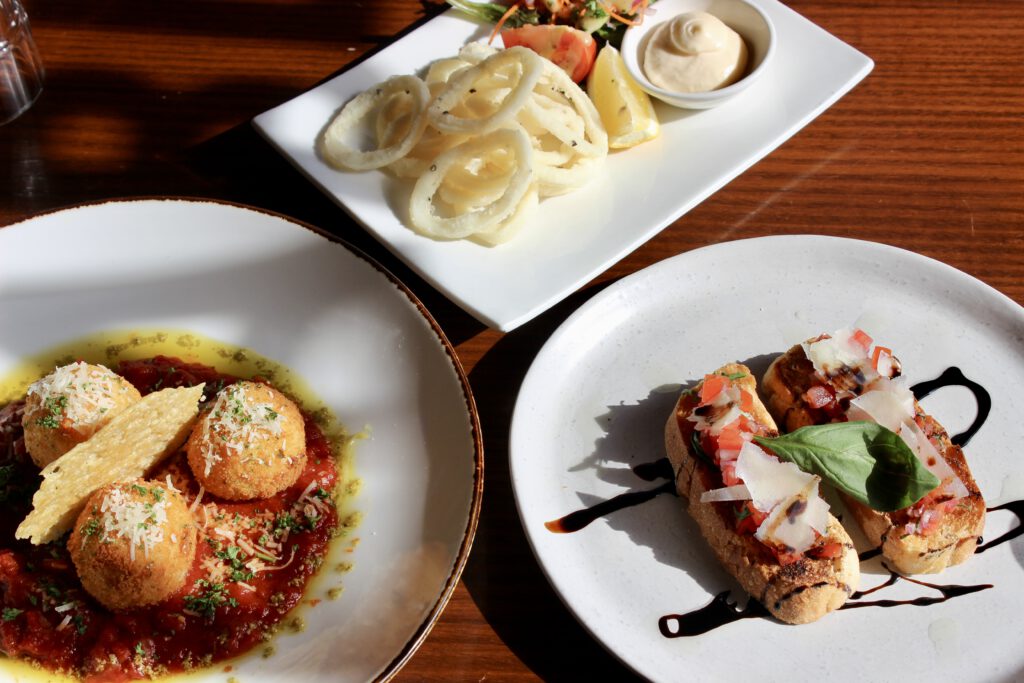 A spread of sharing plates featuring crispy calamari, savory meatballs in sauce, and fresh bruschetta topped with tomatoes and basil, offering a variety of flavors at Table 48.