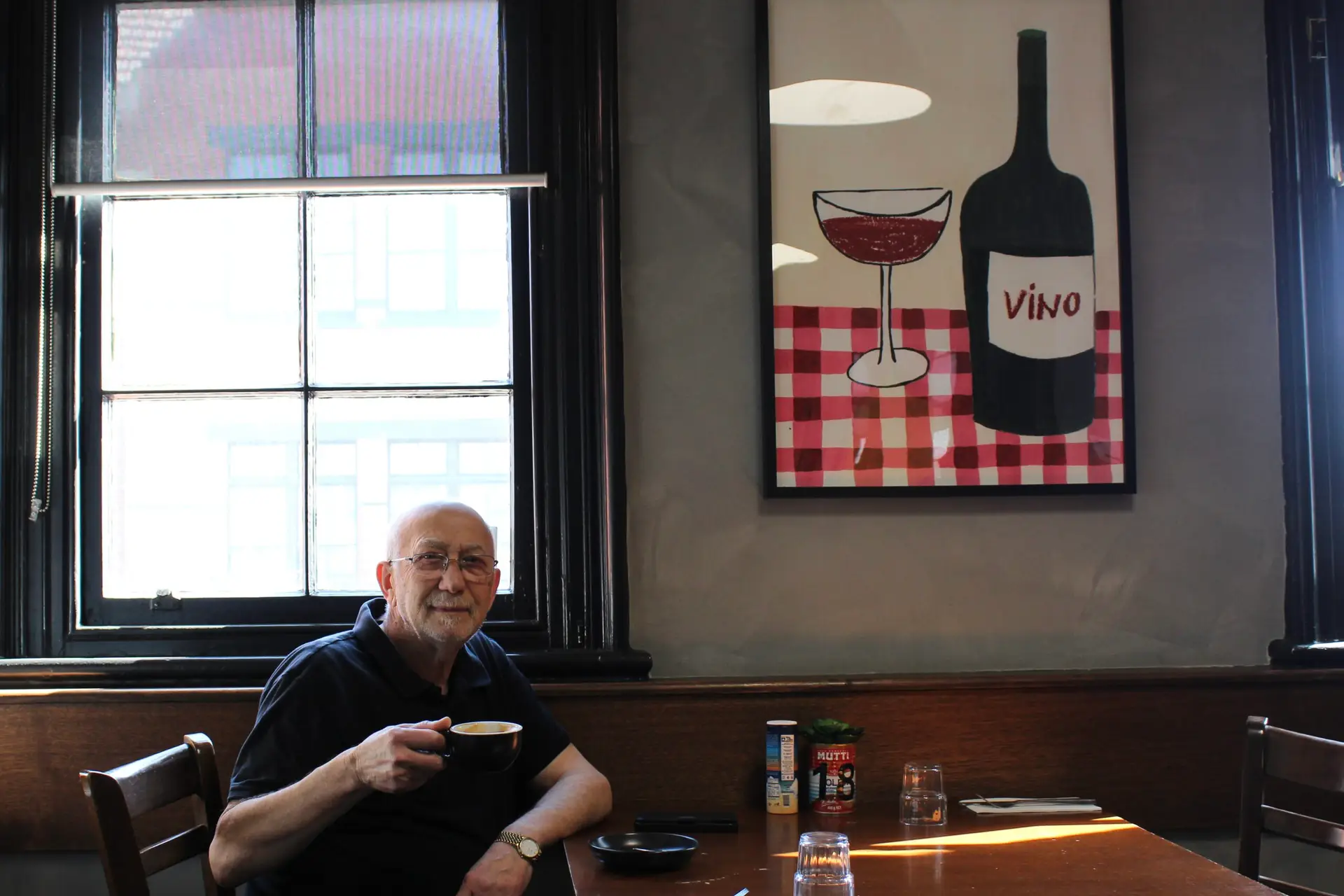 Owner Gus Raschilla sitting comfortably at a table, enjoying a cup of coffee with a relaxed expression, showcasing the inviting atmosphere of Table 48.